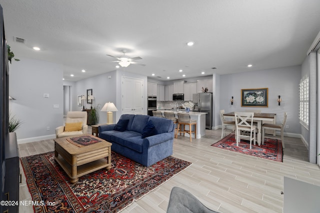 living room with ceiling fan, a textured ceiling, and light hardwood / wood-style flooring