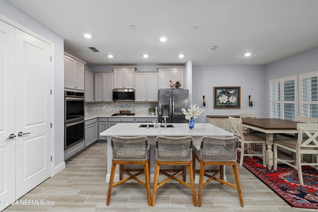 kitchen featuring a kitchen breakfast bar, gray cabinetry, stainless steel appliances, a center island with sink, and sink