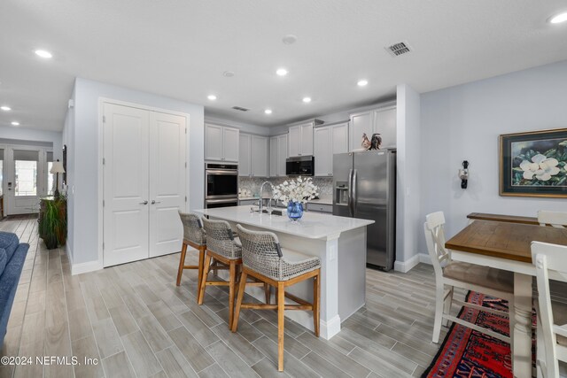 kitchen featuring an island with sink, a kitchen breakfast bar, light hardwood / wood-style floors, stainless steel appliances, and decorative backsplash