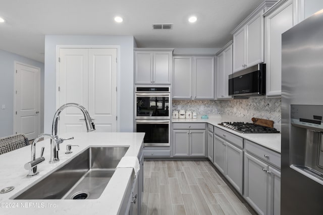 kitchen with gray cabinets, decorative backsplash, stainless steel appliances, and sink