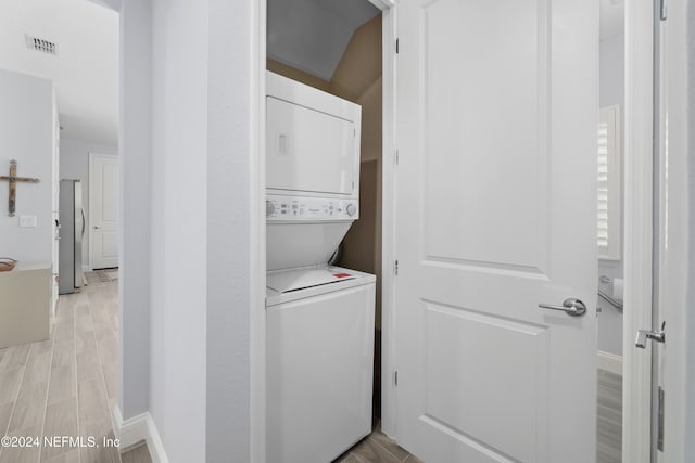 laundry area featuring stacked washer and clothes dryer and light hardwood / wood-style floors