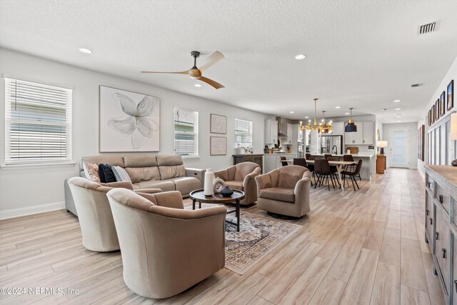 living room featuring light wood-type flooring, a textured ceiling, and ceiling fan with notable chandelier