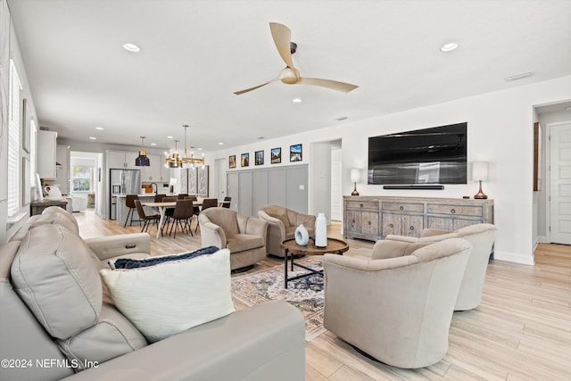 living room with ceiling fan with notable chandelier and light hardwood / wood-style flooring