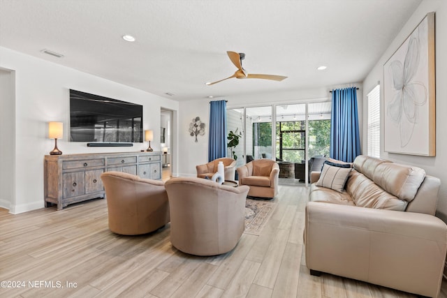 living room with light hardwood / wood-style floors, ceiling fan, and a textured ceiling