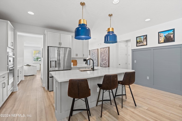 kitchen with sink, appliances with stainless steel finishes, a kitchen island with sink, white cabinets, and light wood-type flooring