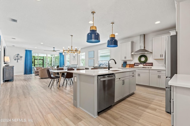 kitchen with pendant lighting, light wood-type flooring, sink, and wall chimney range hood