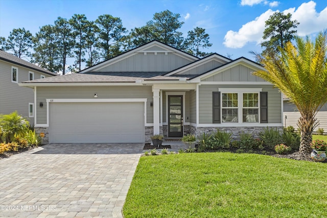 craftsman-style house with decorative driveway, an attached garage, board and batten siding, stone siding, and a front lawn