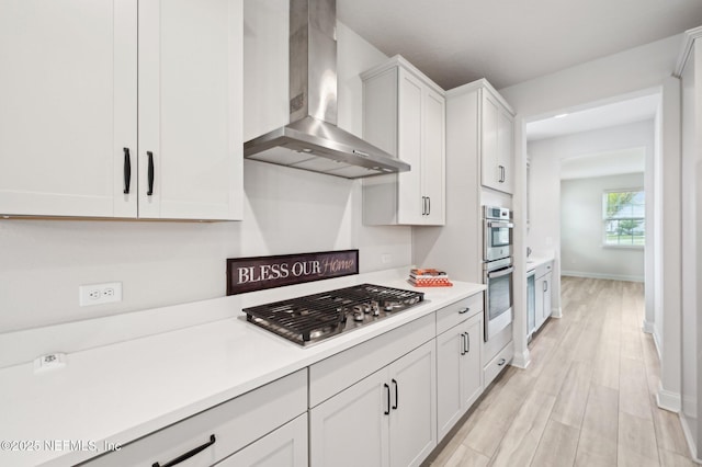 kitchen with light countertops, light wood-style flooring, appliances with stainless steel finishes, white cabinetry, and wall chimney exhaust hood