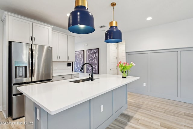 kitchen with stainless steel fridge, light wood-style flooring, light countertops, a decorative wall, and a sink