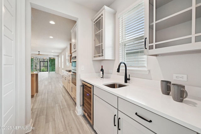 kitchen featuring beverage cooler, light wood-style flooring, glass insert cabinets, a sink, and recessed lighting