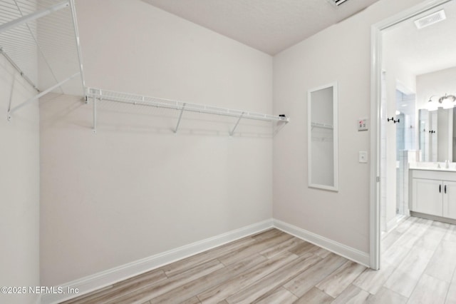 walk in closet featuring light wood finished floors, visible vents, and a sink