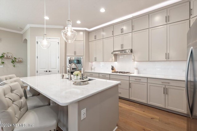 kitchen featuring gray cabinetry, pendant lighting, stainless steel appliances, light hardwood / wood-style flooring, and a center island with sink