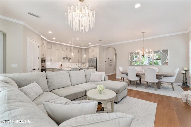 living room featuring a notable chandelier, light hardwood / wood-style flooring, crown molding, and sink