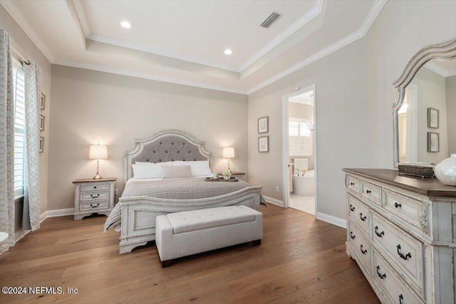 bedroom with a raised ceiling, connected bathroom, ornamental molding, and light hardwood / wood-style flooring