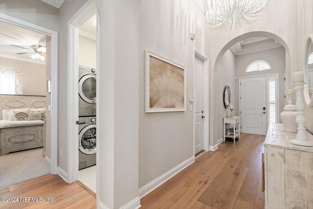 entrance foyer with ceiling fan with notable chandelier, light hardwood / wood-style floors, stacked washer / dryer, and crown molding