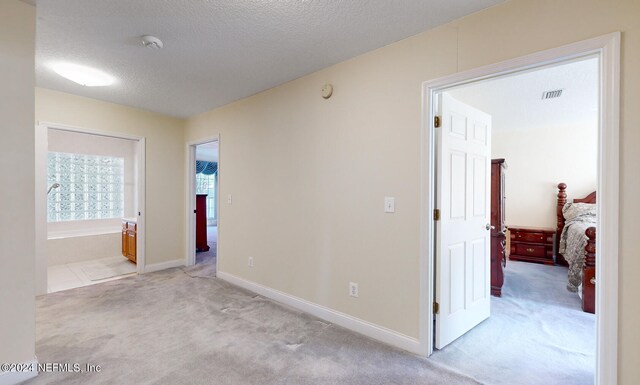 hallway with a textured ceiling and light carpet