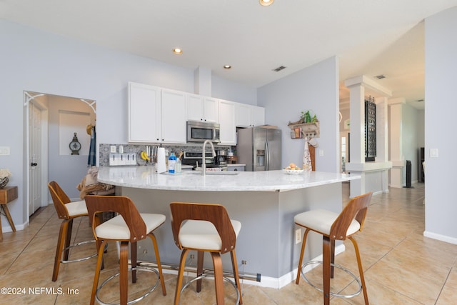 kitchen with light stone counters, kitchen peninsula, stainless steel appliances, a breakfast bar, and decorative backsplash