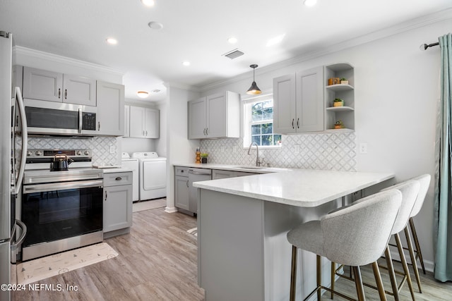 kitchen featuring sink, hanging light fixtures, stainless steel appliances, washing machine and dryer, and kitchen peninsula