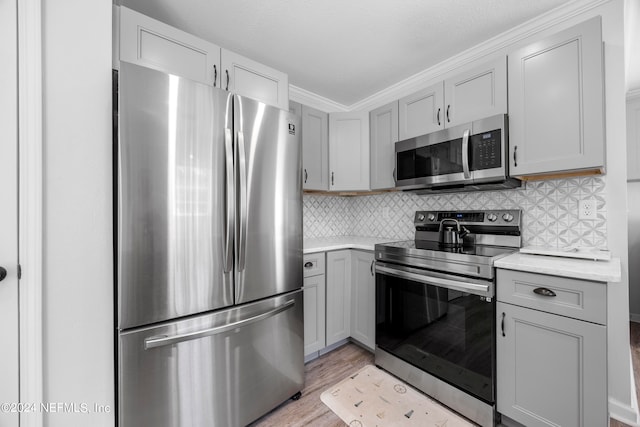 kitchen featuring tasteful backsplash, crown molding, light hardwood / wood-style floors, gray cabinets, and appliances with stainless steel finishes