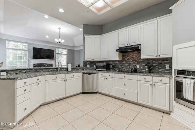 kitchen featuring decorative backsplash, white cabinetry, stainless steel appliances, dark stone counters, and a notable chandelier