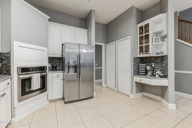 kitchen featuring white cabinets, light tile patterned floors, backsplash, appliances with stainless steel finishes, and light stone countertops