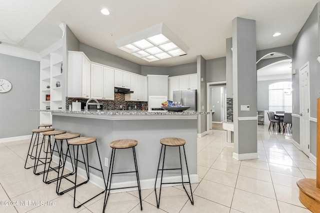 kitchen with light stone counters, white cabinets, kitchen peninsula, stainless steel refrigerator, and decorative backsplash