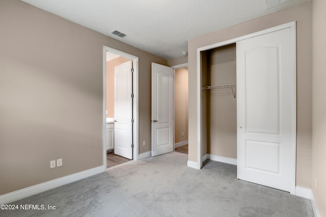 unfurnished bedroom featuring light carpet, a closet, ensuite bathroom, and a textured ceiling