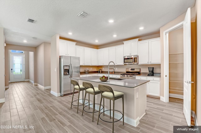 kitchen with sink, light wood-type flooring, stainless steel appliances, and an island with sink