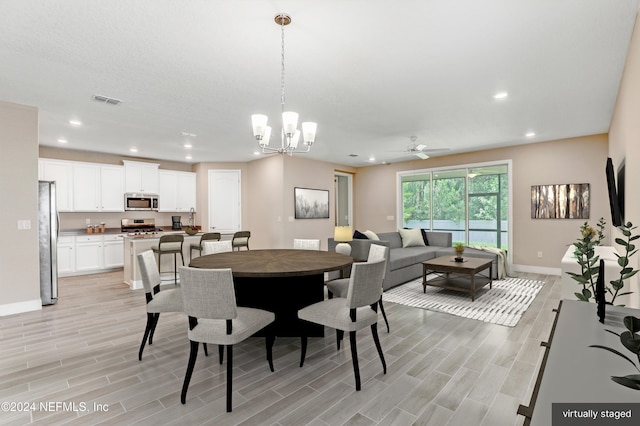 dining space featuring ceiling fan with notable chandelier and light wood-type flooring