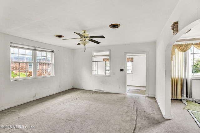 carpeted spare room with a wealth of natural light, arched walkways, and visible vents