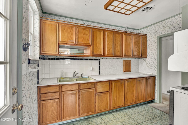 kitchen with wallpapered walls, brown cabinets, a sink, and light countertops