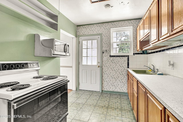 kitchen featuring brown cabinets, stainless steel microwave, electric range, a sink, and wallpapered walls