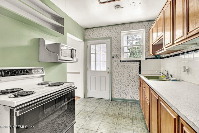 kitchen with range with electric stovetop, a sink, brown cabinetry, stainless steel microwave, and wallpapered walls