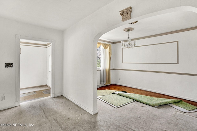 carpeted spare room with arched walkways, ornamental molding, baseboards, and a notable chandelier