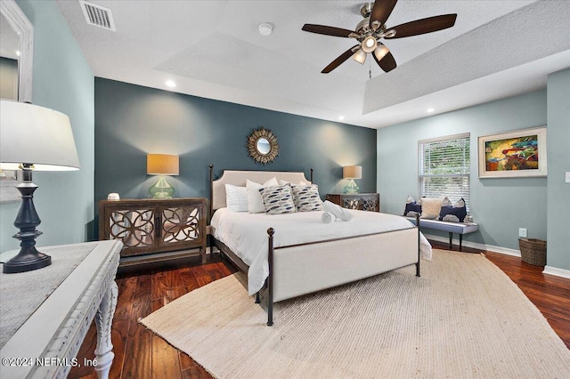 bedroom with ceiling fan, a textured ceiling, a raised ceiling, and dark hardwood / wood-style floors