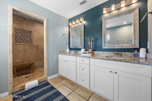 bathroom featuring a textured ceiling, a tile shower, and vanity