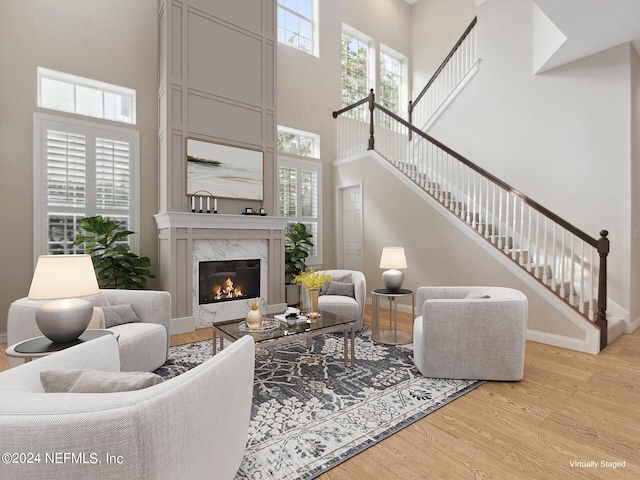 living room featuring light hardwood / wood-style floors, a towering ceiling, and a high end fireplace