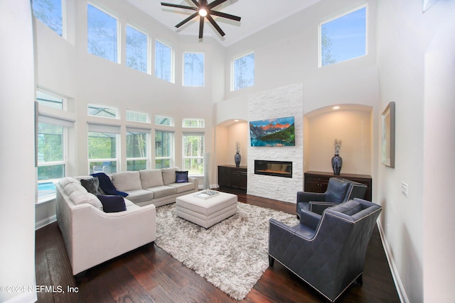 living room featuring ceiling fan, a stone fireplace, dark hardwood / wood-style floors, and plenty of natural light