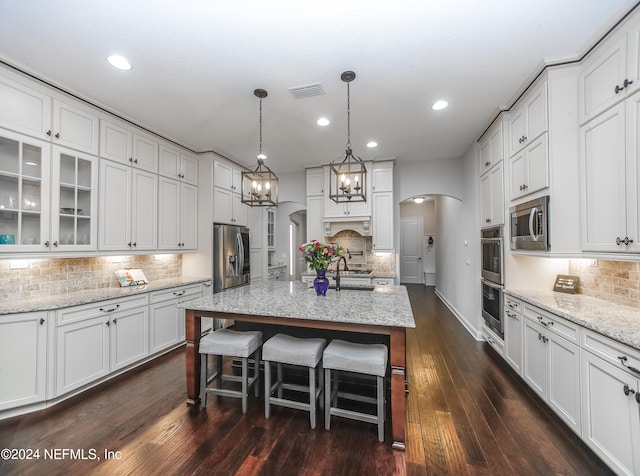 kitchen featuring a chandelier, dark hardwood / wood-style floors, a kitchen island with sink, white cabinets, and appliances with stainless steel finishes