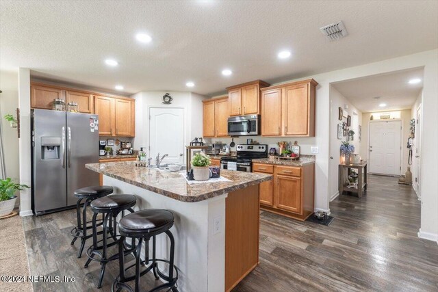 kitchen with stainless steel appliances, a center island with sink, a textured ceiling, and dark hardwood / wood-style flooring