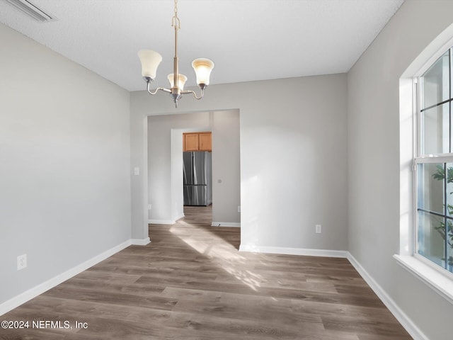 unfurnished dining area with dark hardwood / wood-style flooring, a textured ceiling, and a notable chandelier