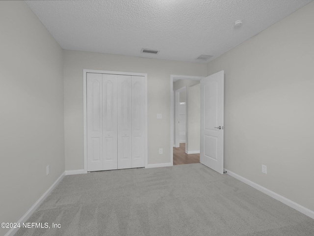 unfurnished bedroom with a textured ceiling, light carpet, and a closet