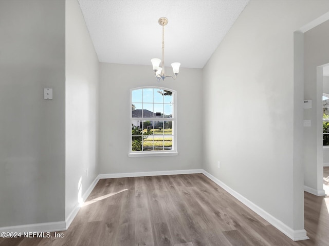 unfurnished dining area featuring light hardwood / wood-style floors, a textured ceiling, and an inviting chandelier