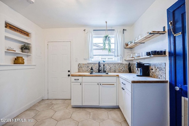 kitchen with sink, decorative light fixtures, butcher block countertops, white cabinetry, and light tile patterned flooring