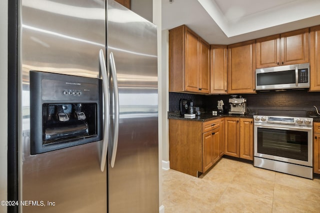 kitchen featuring light tile patterned floors, backsplash, stainless steel appliances, and dark stone counters