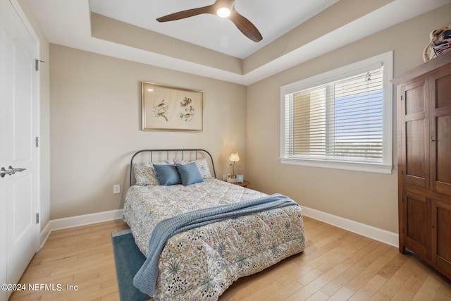 bedroom with a tray ceiling, ceiling fan, and light hardwood / wood-style flooring