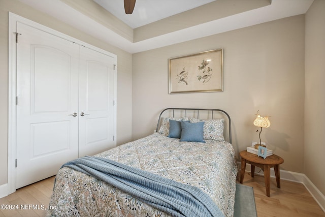 bedroom featuring a raised ceiling, ceiling fan, a closet, and light wood-type flooring