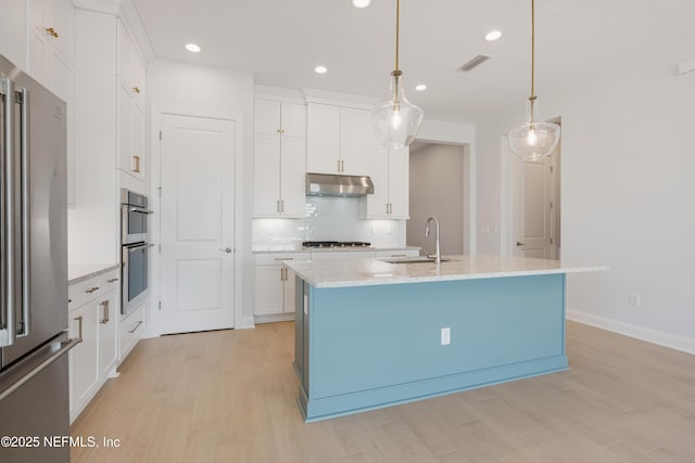 kitchen with stainless steel appliances, sink, white cabinetry, hanging light fixtures, and an island with sink