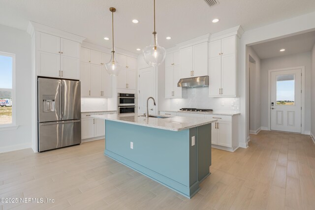 kitchen featuring stainless steel appliances, a kitchen island with sink, sink, white cabinets, and hanging light fixtures