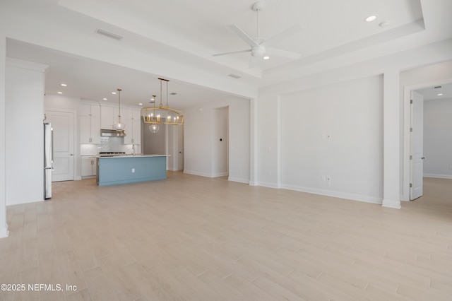 unfurnished living room with ceiling fan with notable chandelier and a raised ceiling